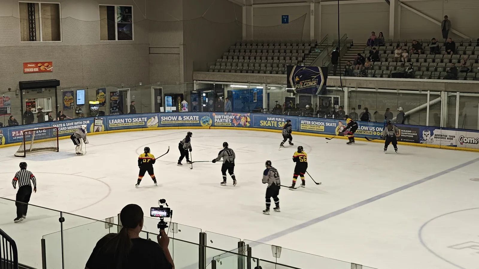 A phone on a tripod in the arena stands, broadcasting a local hockey game live to YouTube with BenchStream